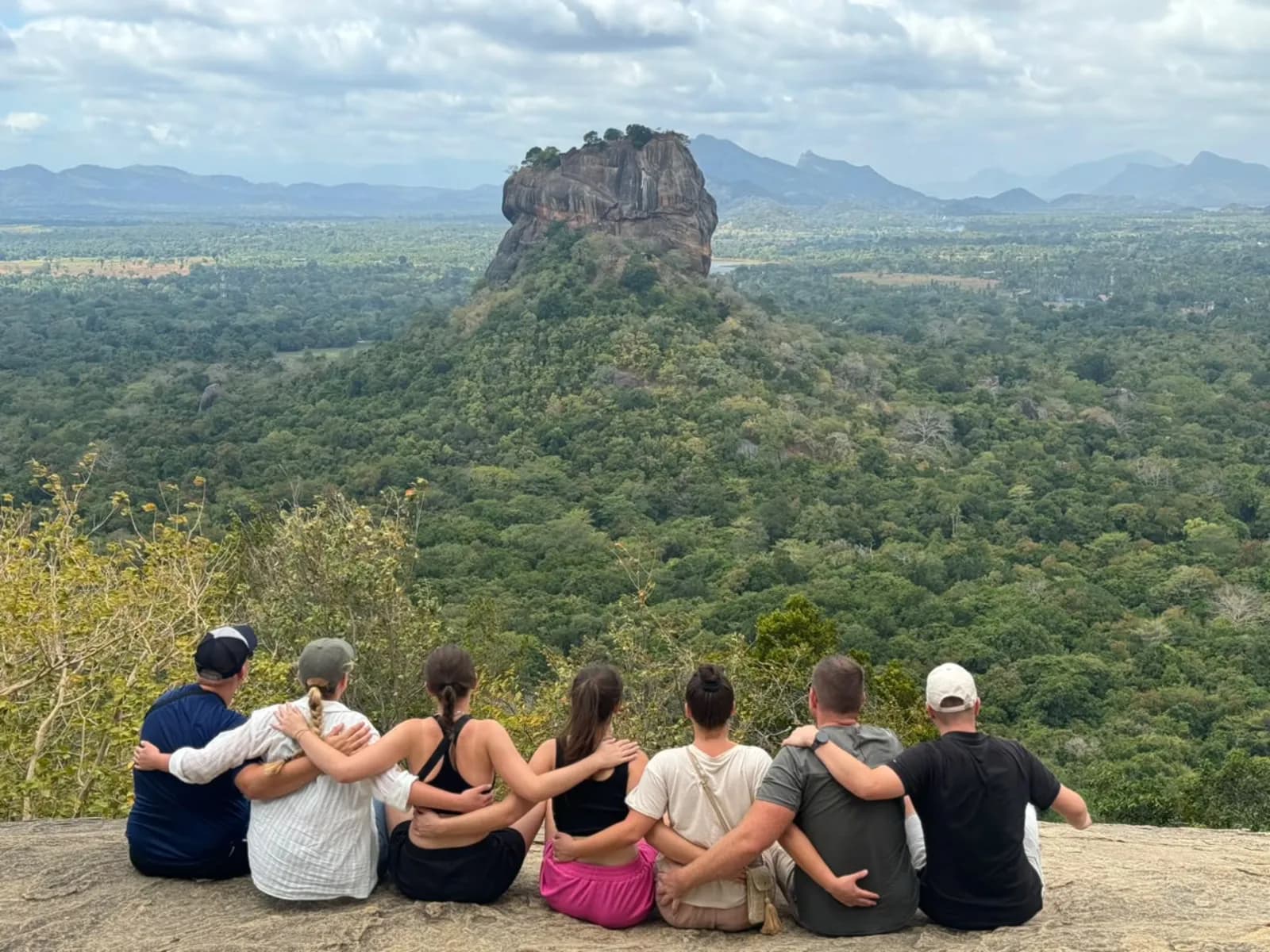 Travellers sitting on Pidurangala rock looking across the jungle to Sigiriya